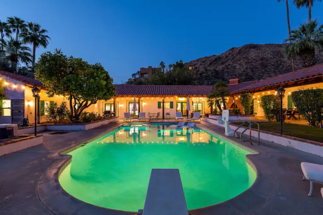 A swimming pool with lounge chairs and a building with lights in the background.