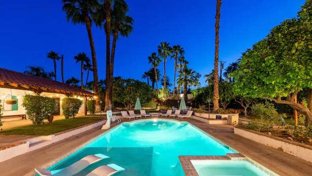 A swimming pool with lounge chairs and umbrellas, surrounded by palm trees and a building with a red-tiled roof. - Spacious 4BR Historic Spanish Estate/Pool,Casita & Mountain Views/Old Las Palmas (Palm Springs)