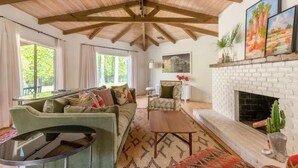 A spacious living room with a high ceiling, a fireplace, and a large window. - Spacious 4BR Historic Spanish Estate/Pool,Casita & Mountain Views/Old Las Palmas (Palm Springs)