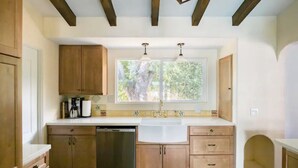 A kitchen with wooden cabinets, a dishwasher, and a window with a view of greenery. - Spacious 4BR Historic Spanish Estate/Pool,Casita & Mountain Views/Old Las Palmas (Palm Springs)