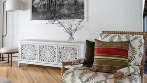 A cozy living room with a patterned armchair, a white cabinet, and a framed black and white mountain painting. - Spacious 4BR Historic Spanish Estate/Pool,Casita & Mountain Views/Old Las Palmas (Palm Springs)