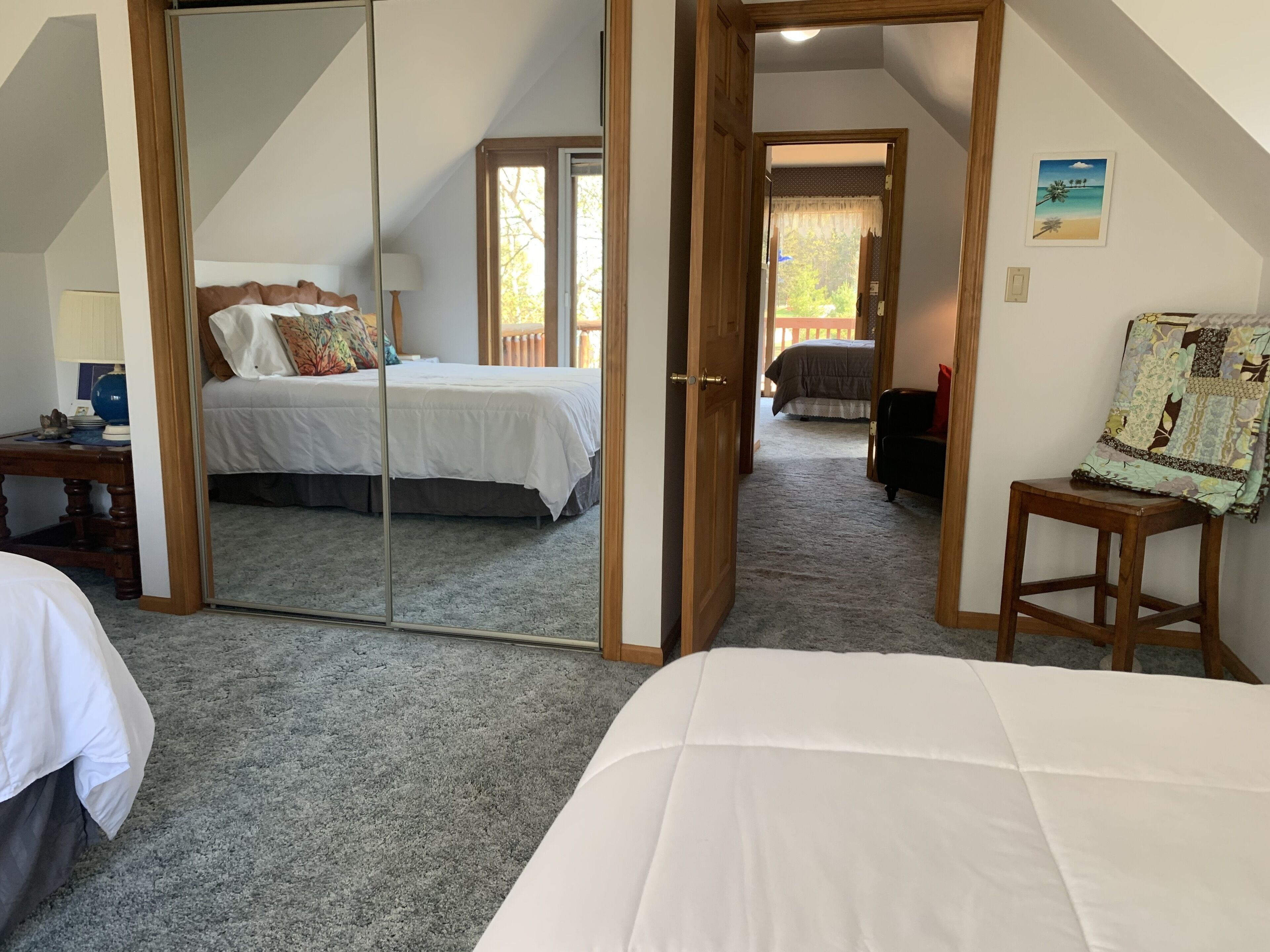 A bedroom with a large mirror, a bed with white bedding, a wooden chair, and a small table.