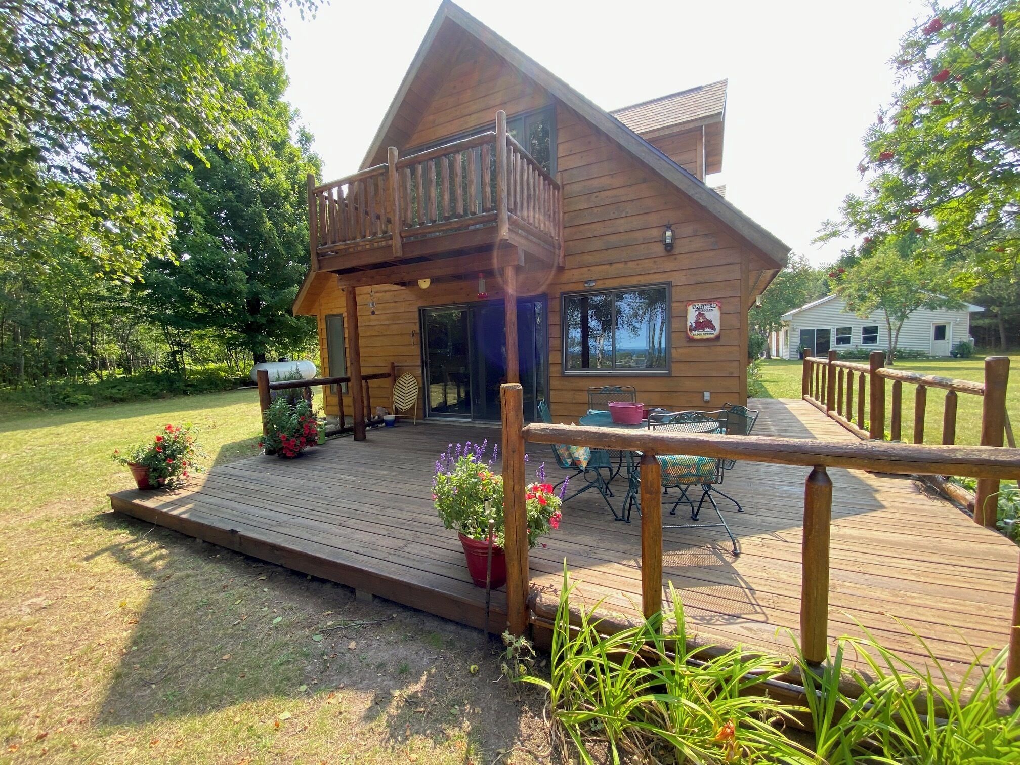 A wooden cabin with a deck, outdoor seating, and a view of the surrounding greenery.