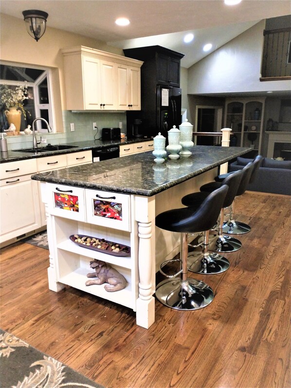 Een moderne keuken met witte kasten, een granieten aanrechtblad en een centraal kookeiland met barstoelen.