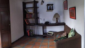 A cozy room with a wooden ceiling, a brown sofa, a radiator, a shelf with books, and a framed picture on the wall.