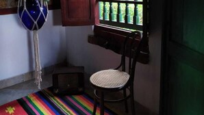 A room with a wooden chair, a colorful striped rug, a macrame hanging, and a window with green bars.