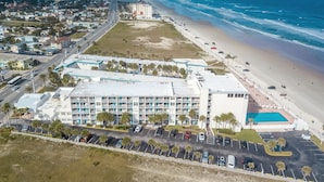 Vista aérea de un hotel con estacionamiento, playa y océano.