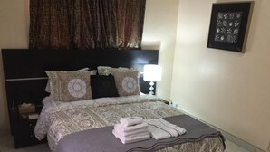 Ein ordentlich bezogenes Bett mit einer gemusterten Tagesdecke, ein Stapel gefalteter Handtücher und eine Nachttischlampe.
