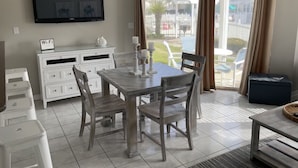Un espace repas avec une table et des chaises, un téléviseur fixé au mur, un panneau indiquant la présence d’une connexion Wi-Fi, et une vue sur l’extérieur à travers une porte vitrée.