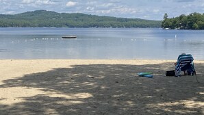 Una playa con una orilla arenosa, una masa de agua y una colina boscosa al fondo.