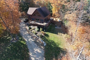 A two-story log cabin with a deck, surrounded by a wooded area with autumn foliage.