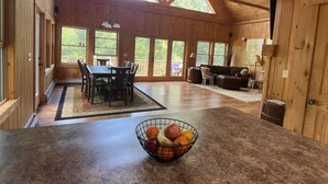 Una cabaña de madera espaciosa con comedor, sala de estar y cocina, con un frutero sobre la encimera.