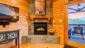 A cozy cabin interior with a stone fireplace, wooden walls, a mounted television, and a sign above the fireplace.