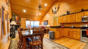 A cozy log cabin interior with a dining area, kitchen, and fireplace.