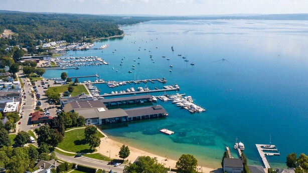 Vue aérienne d’une marina où sont amarrés de nombreux bateaux, d’une plage de sable et des quartiers résidentiels environnants.