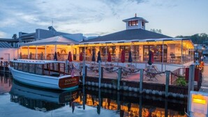 Un restaurant situé au bord de l’eau, avec un bateau amarré, des tables en plein air et un espace couvert.