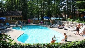 Une piscine entourée d’arbres et d’un mur de pierre, avec des chaises longues et des parasols à proximité.