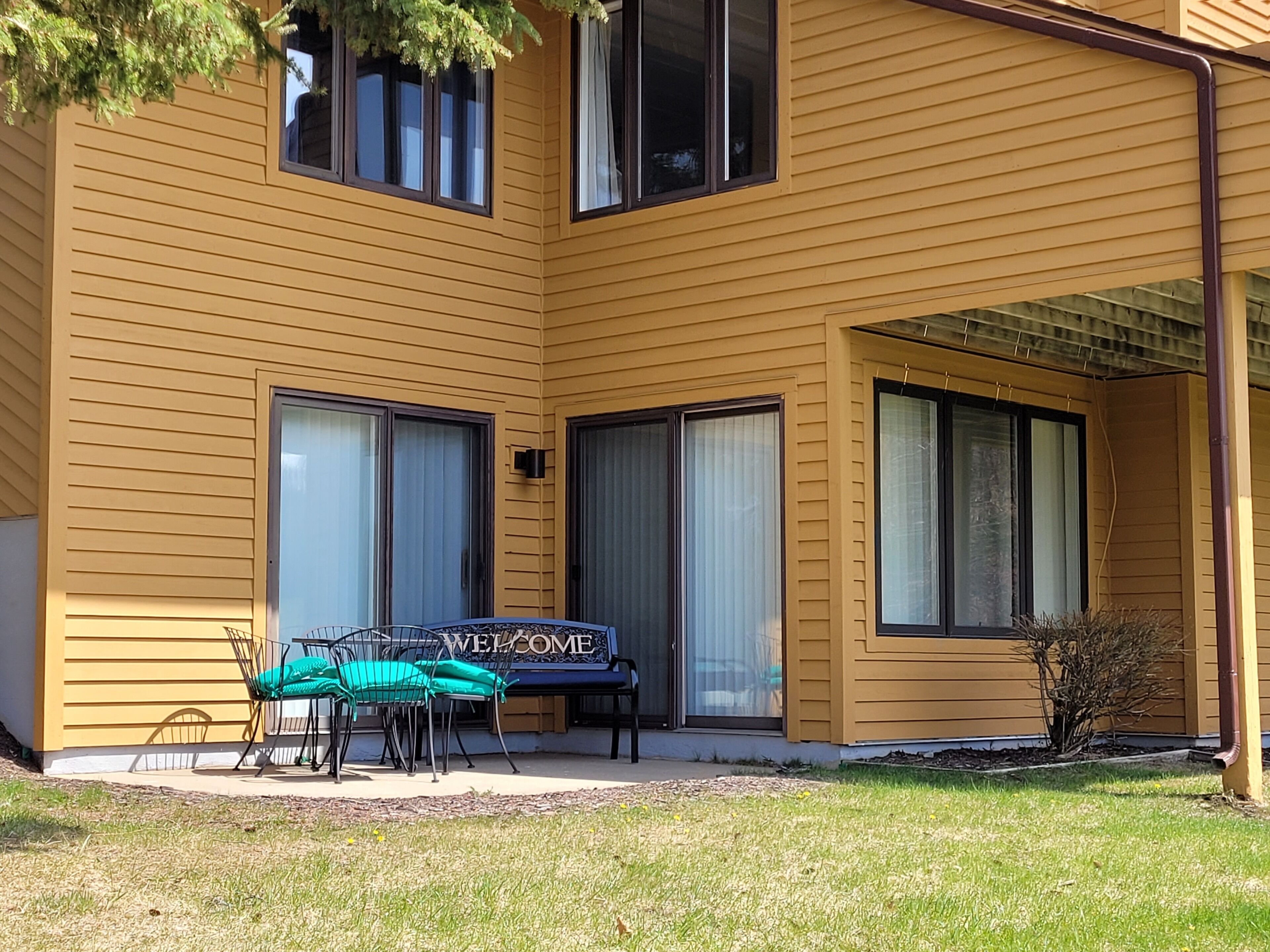 A yellow building with a patio area featuring a table and chairs, a welcome sign, and large windows.