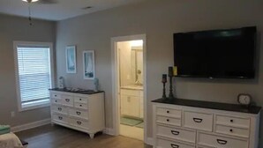 Une chambre à coucher avec un lit, une commode, un téléviseur et une salle de bain visible à travers une porte ouverte.