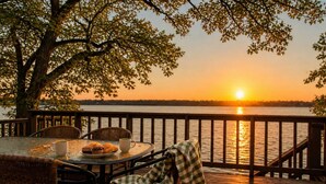 A deck with a table set for breakfast, overlooking a body of water at sunset. - SPACIOUS and Stylish Lakefront Retreat, STUNNING Views, Firepit! (Fox Lake)