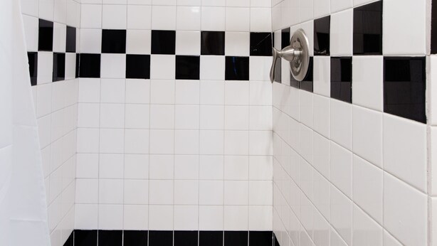 A bathroom with white tiles and black accents, a showerhead, and a bathtub. - SPACIOUS and Stylish Lakefront Retreat, STUNNING Views, Firepit! (Fox Lake)
