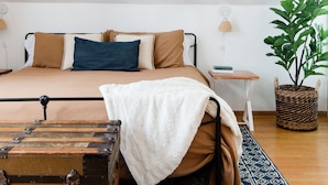 A bedroom with a bed, a nightstand, a lamp, a potted plant, and a suitcase. - SPACIOUS and Stylish Lakefront Retreat, STUNNING Views, Firepit! (Fox Lake)