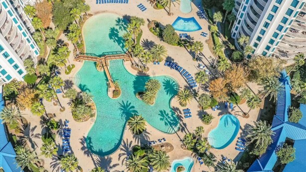 Vista aerea di un resort con diverse piscine, palme e zone spiaggia.