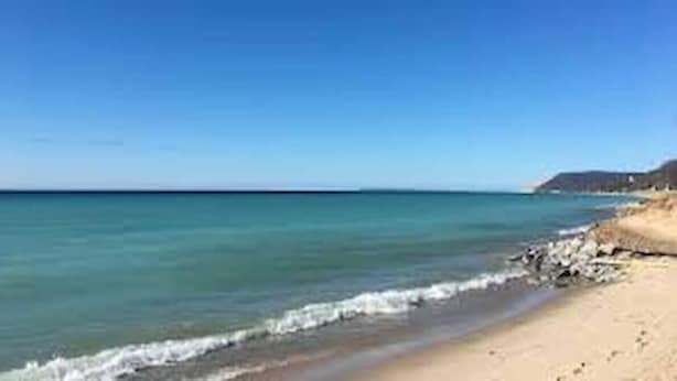 Een strand met helder water, een zandstrand en een heuvel in de verte.