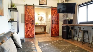 Een gezellige woonkamer met een bank, een televisie en een keukenhoek met een schuifdeur.