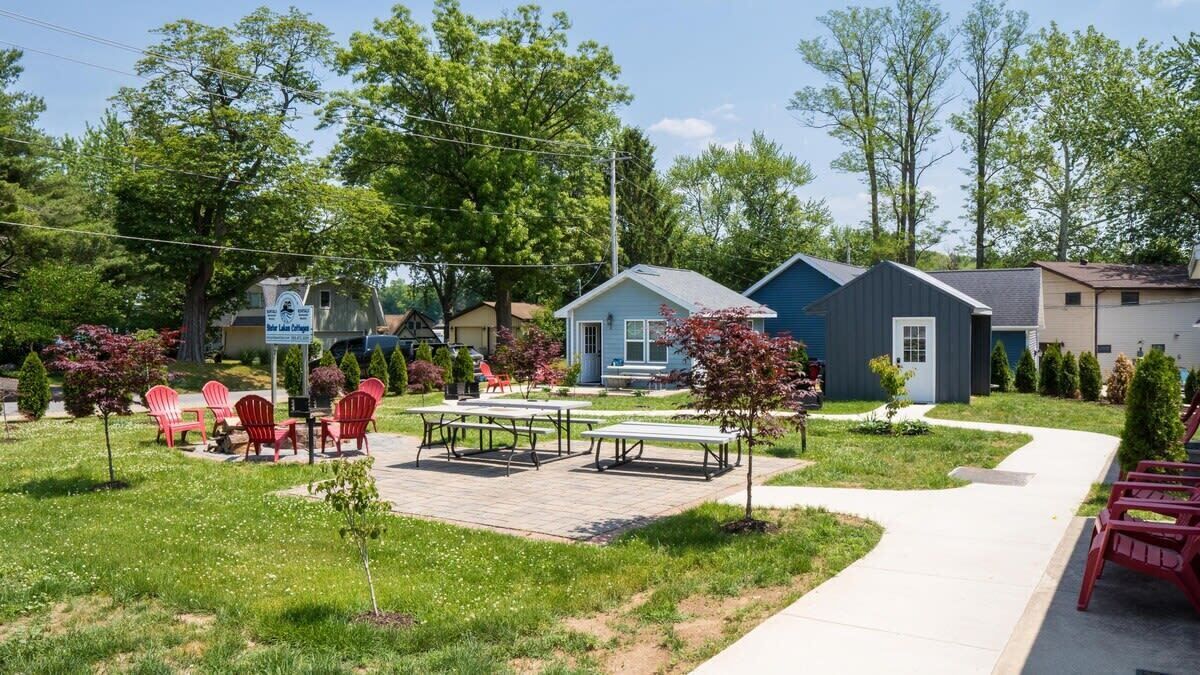 A courtyard with picnic tables and chairs, surrounded by small houses with a sign indicating a rental property.
