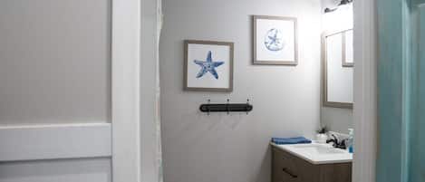 A bathroom with a white wall, a framed starfish picture, a framed flower picture, a black towel rack, a wooden cabinet, and a mirror.