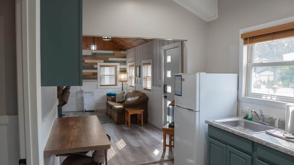 A compact kitchen with a wooden table, a sofa, and a refrigerator.