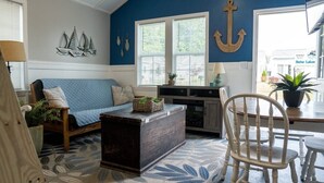 Uma sala de estar aconchegante com um sofá azul, mesa de centro de madeira e um espaço de jantar com uma cadeira branca.