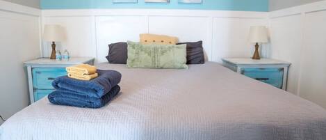 A neatly made bed with folded towels, two bedside tables with lamps, and a wall with three framed pictures.