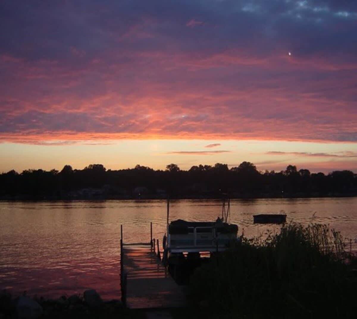 A sunset over a calm lake with a dock and a boat.