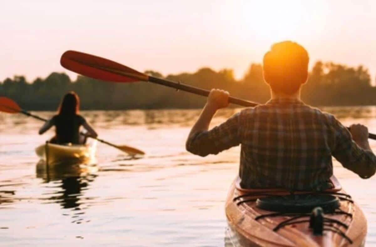 Twee personen kajakken op een rustig wateroppervlak tijdens de zonsondergang.
