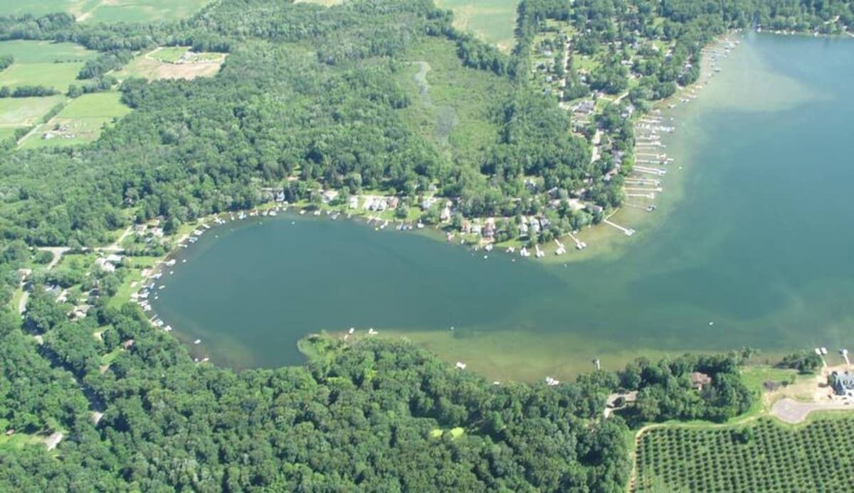 An aerial view of a lake surrounded by dense forest and a small settlement with boats docked along the shore.
