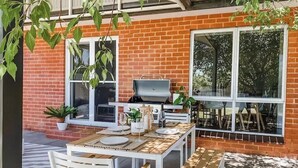 An outdoor patio with a wooden table set for dining, a barbecue grill, and potted plants. - Stylish duplex in Prime Location! (Wagga Wagga)