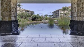 A covered walkway with stone pillars, leading to a pool area with water and greenery. - 2 Bedroom 3 bath in Waipouli Deluxe oceanfront condominium Resort (Kapaa)