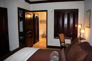 Ein Hotelzimmer mit Bett, Stuhl, Schreibtisch mit Lampe, Kleiderschrank und einer Tür zum Badezimmer.