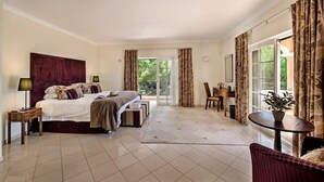 Een ruime slaapkamer met een groot bed, een zithoek met een tafel en stoelen, en uitzicht op de omgeving door een schuifdeur.