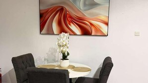 Ein Essbereich mit einem runden Tisch, vier Stühlen, einer Blumenvase und einem großen abstrakten Gemälde an der Wand.