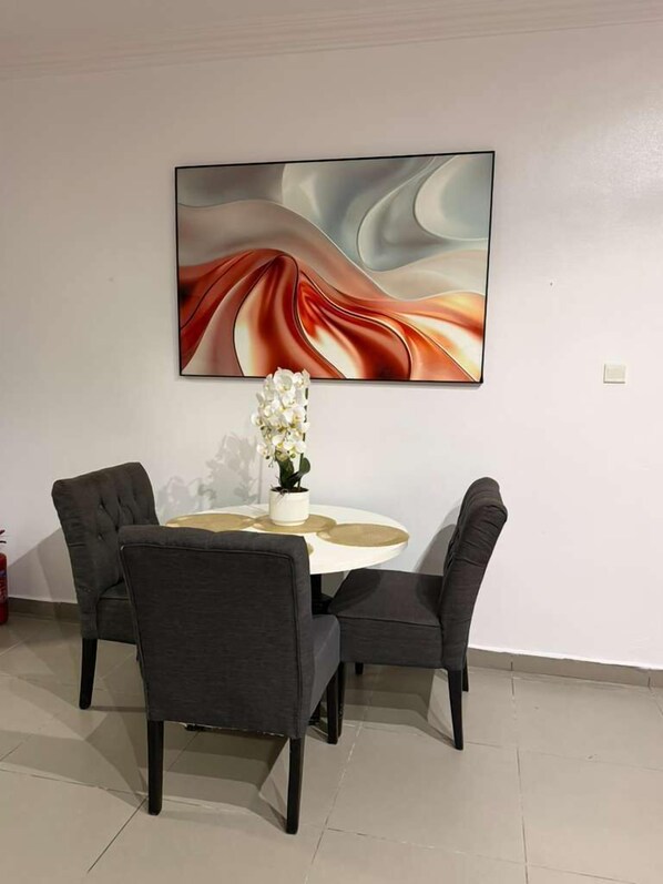 A dining area with a round table, four chairs, a vase of flowers, and a large abstract painting on the wall.