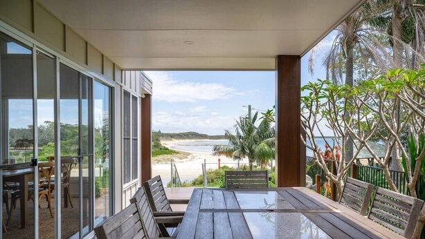 Une terrasse en bois dotée d’une balustrade en verre, qui offre une vue sur la plage.