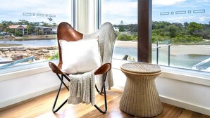 Une pièce avec vue sur la plage et la mer, une chaise en osier avec un coussin et une petite table ronde.