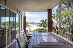 Une terrasse en bois dotée d’une balustrade en verre, qui offre une vue sur la plage.