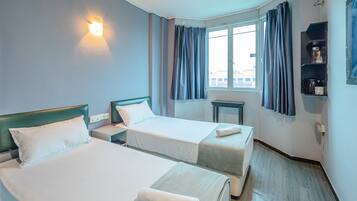 Habitación de hotel con dos camas, una mesita de noche, una ventana con cortinas y un estante con cafetera.