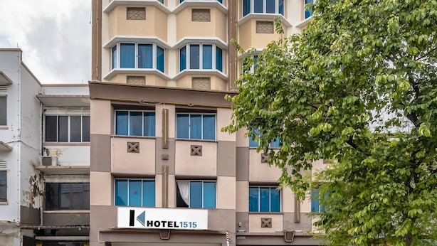 A multi-story hotel with a classic architectural design, featuring a prominent entrance with a sign, and a large tree in the foreground. - K Hotel 1515 (Singapore)
