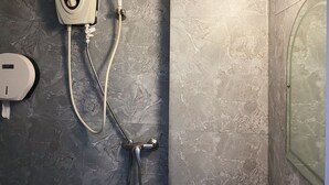A bathroom with a handheld showerhead, a wall-mounted faucet, and a soap dispenser. - K Hotel 1515 (Singapore)