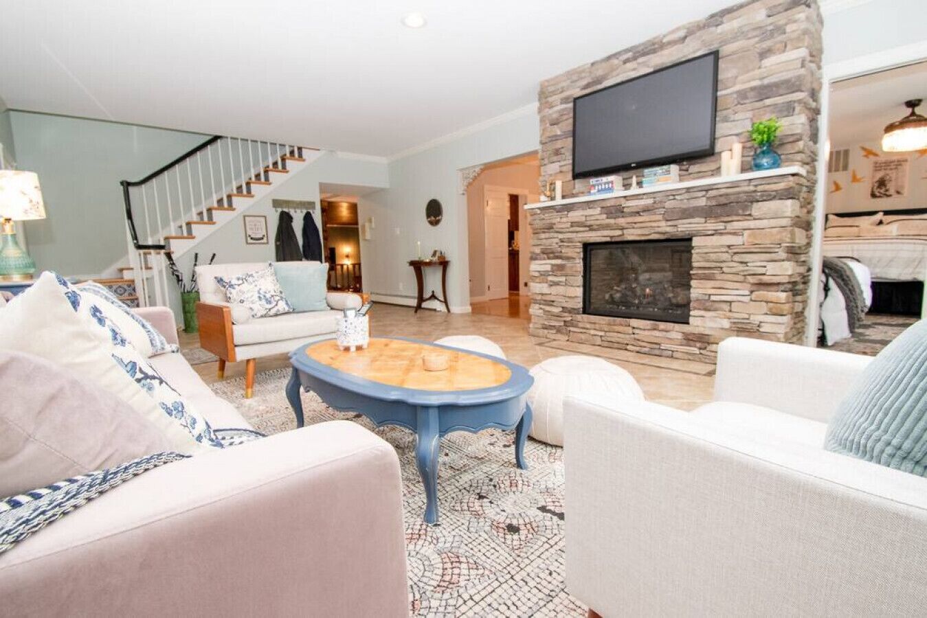 A living room with a stone fireplace, a flat-screen TV mounted above it, and a staircase leading to another level.